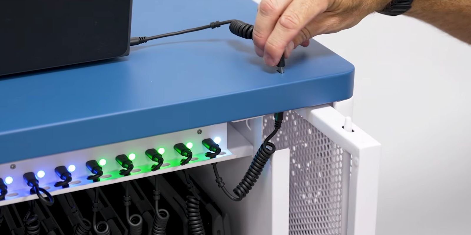 Close-up of a person connecting a USB-C charging cable to a JAR Systems charging cart with LED charging status indicators.