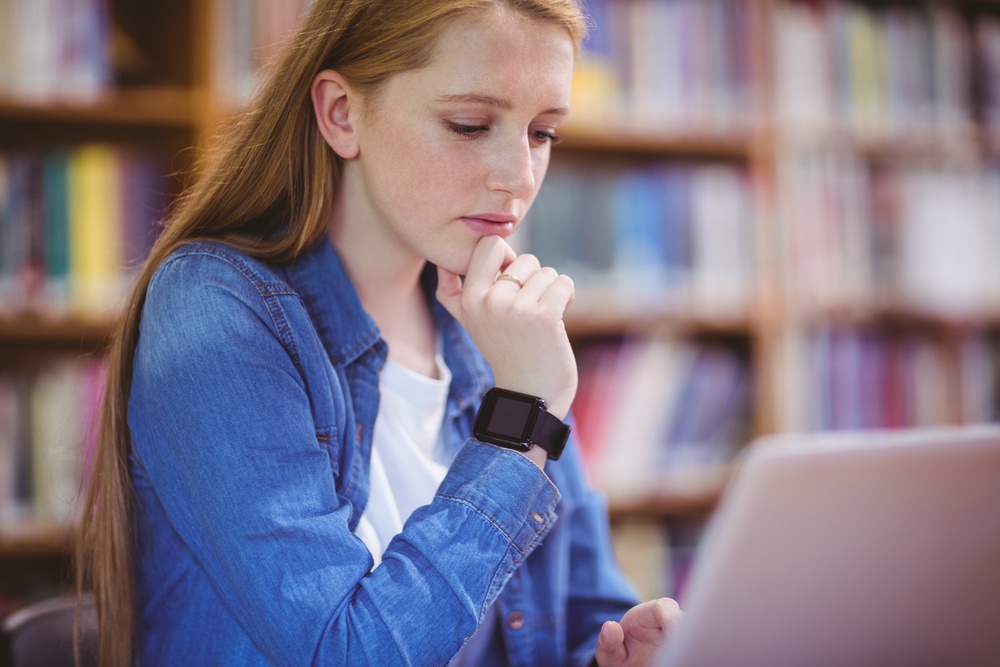Student with smartwatch using laptop in library at the university