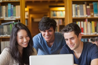 Students sitting looking at a laptop at the library